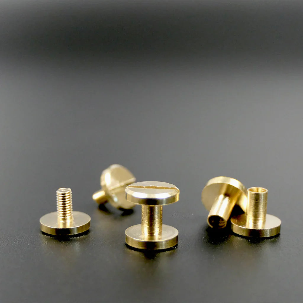 Solid brass Chicago screws with flat heads, arranged on a matte black surface.