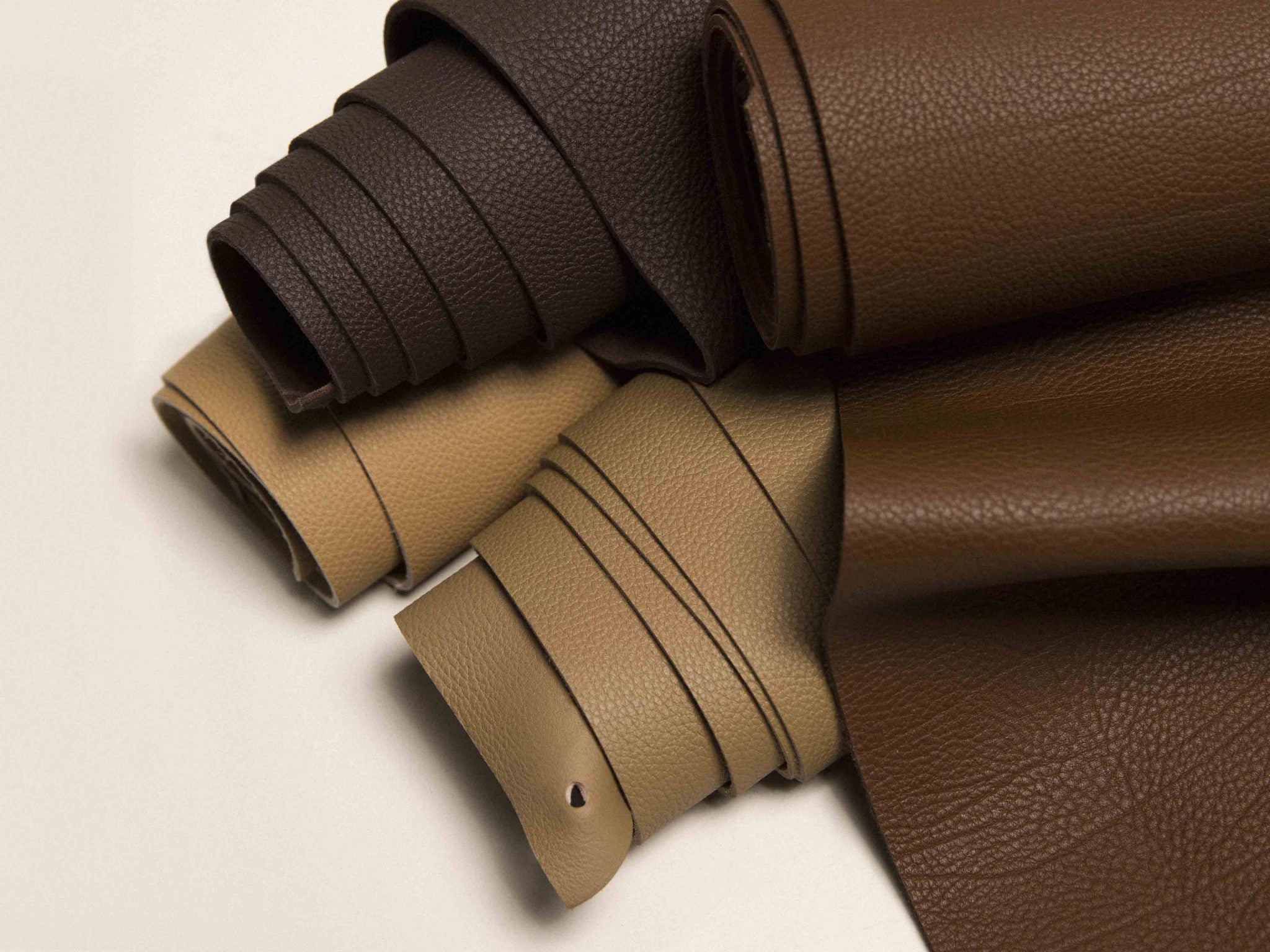 Rolled full-grain leather hides in brown and beige tones, premium materials for crafting luxury bags, wallets, and fine leather goods
