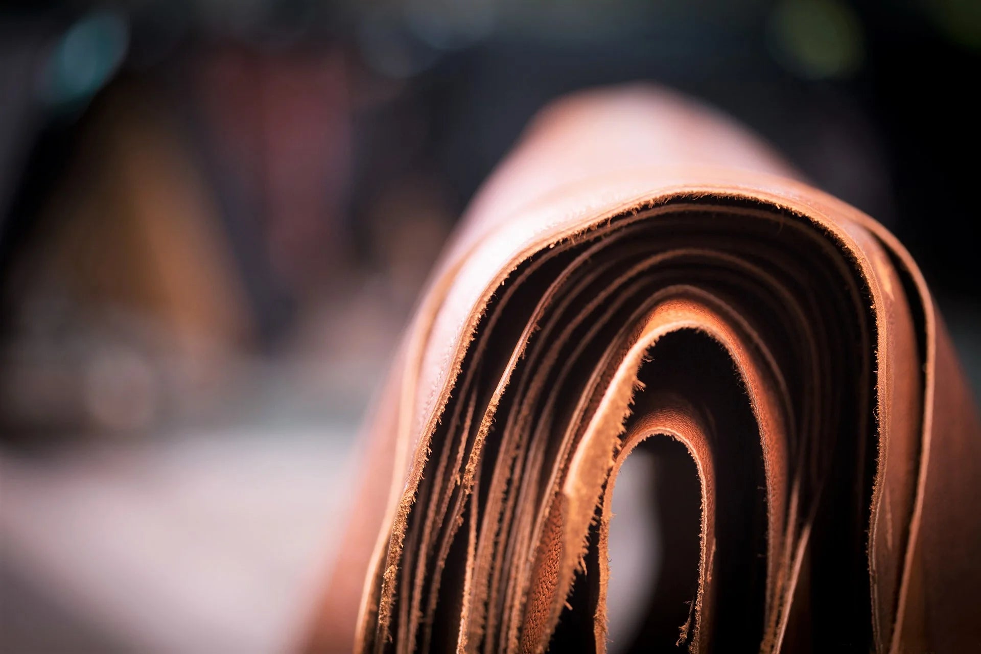 Stacked full-grain calf leather hides in natural tones, showing premium texture and clean cut edges in a leathercraft workshop